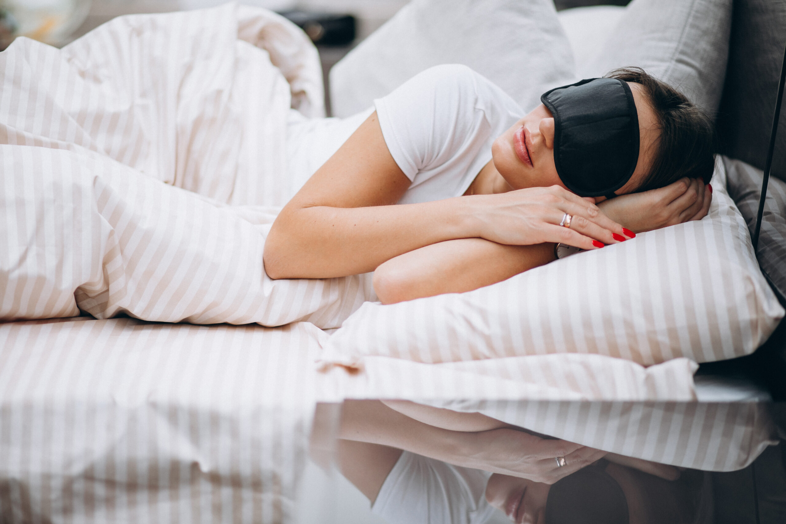 Young woman resting in bed in the morning, lying on white sheets with a peaceful expression.

